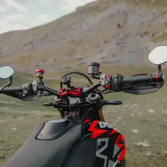 Manubrio di una moto con specchietti bar end, pronto per un'avventura tra le montagne.
