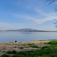 Spokojna tafla wody w Dolinie Bystrzycy, idealna na spacer po szlakach pieszych. Dwie osoby odpoczywają na piaszczystym brzegu.