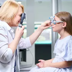 Ortoptysta bada wzrok dziewczynki, która ma założony aparat do badania refrakcji.