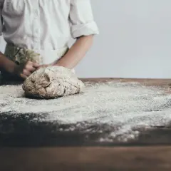 Dziecko w fartuszku przygotowuje ciasto na stole. Zastanawiasz się, jaka mąka jest najzdrowsza? Ta na zdjęciu wygląda na pełnoziarnistą.