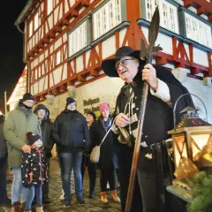 Ein Nachtwächter mit Hellebarde und Laternen auf dem Vellberg Weihnachtsmarkt. Besucher in Weihnachtsmützen und warmen Jacken stehen davor.