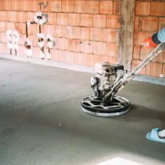 Pracownik wykonuje zacieranie betonu za pomocą mechanicznej zacieraczki.