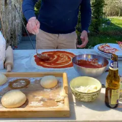Przygotowanie pizzy w słonecznym Chianti, Włochy. Ciasto, sos pomidorowy i ser czekają na pieczenie.