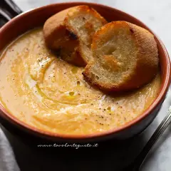 Una ciotola di terracotta contiene una vellutata crema di fagioli cannellini, guarnita con crostini dorati e un filo d'olio.