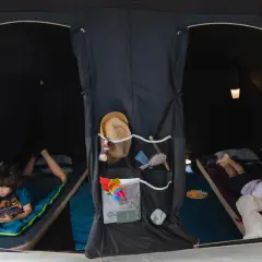 Dzieci cieszą się **campingiem dla dzieci** w namiocie. Chłopiec czyta książkę, dziewczynka bawi się z pluszakiem.