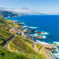 Costa de Tenerife con pueblo colorido, mar azul y el Teide al fondo. ¡Perfecto para tus viajes a Tenerife todo incluido 2x1!