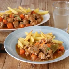 Dos platos de estofado de cerdo con patatas fritas y zanahorias, servidos en una mesa de madera.