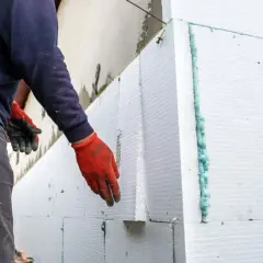 Operaio con guanti rossi applica pannelli per cappotto termico su intonaco esistente.