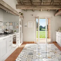 Cucina rustica con pavimento decorato, pensili bianchi e un'ampia porta finestra che si apre su un prato verde. La posa battiscopa è curata nei dettagli.