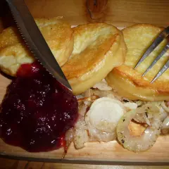 Usmażony oscypek z żurawiną, cebulą i sztućcami na desce.