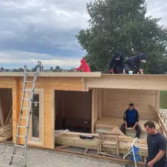 Arbeiter erneuern das **Gartenhaus Dach**. Eine Leiter steht bereit, während mehrere Personen auf dem Dach arbeiten.