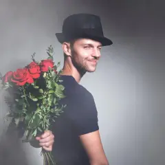 Elegancki mężczyzna w kapeluszu trzyma bukiet czerwonych róż za plecami. Idealny prezent na imieniny Marcina.