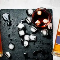 Dwie butelki, szklanka z lodem i ciemnym płynem. Ilustruje różnicę między whisky a whiskey oraz bourbonem a scotchem.