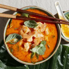 Aksamitna zupa tom yum z krewetkami, świeżą bazylią i kolendrą, podana z pałeczkami i łyżką.