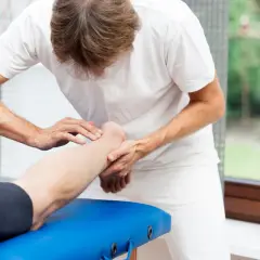 Fizjoterapeuta delikatnie masuje łydkę pacjenta, wspierając rehabilitację po zerwaniu ścięgna Achillesa.