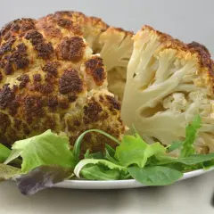 Coliflor al horno, dorada y tierna, servida con una fresca ensalada verde. Un plato saludable y delicioso.