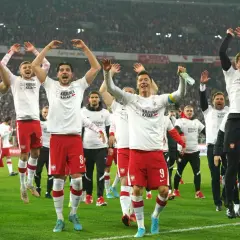 Piłkarze reprezentacji Polski w białych koszulkach i czerwonych spodenkach świętują na boisku.