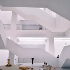Nowoczesne muzeum sztuki z białymi, geometrycznymi schodami i kilkoma zwiedzającymi.