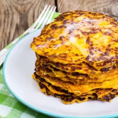 Stos placków z marchewki na talerzu, obok widelca i zielonego ręcznika.