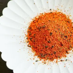A pile of vibrant Japanese 7 spice blend, featuring chili flakes and black sesame seeds, sits on a white, fluted dish.