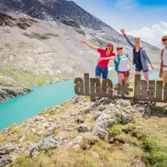 Quatre amis profitent de leurs vacances d'été dans les Alpes, près d'un lac turquoise. Ils posent devant un panneau "alpe d'huez".