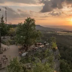 Widok z tarasu restauracji na Górach Stołowych o zachodzie słońca. Drewniany taras z meblami, otoczony skalistym zboczem i lasem.