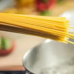 Dłoń trzymająca spaghetti nad gotującą się wodą. Zastanawiasz się, jaki makaron ma najmniej kalorii?