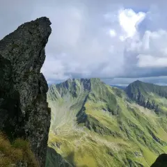 Steile Felsformationen und grüne Berghänge im Rahmen einer **Karpaten Wanderung**. Dramatische Wolkenformationen über den Gipfeln.