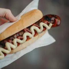 Kabanos w bułce z keczupem i musztardą, trzymany w dłoni.