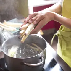 Hände legen weißen Spargel in kochendes Wasser. So wird gefrorener Spargel kochen.