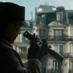 Mężczyzna w kapeluszu i rękawiczkach obserwuje coś przez lornetkę. Klimat jak z filmów Davida Finchera.