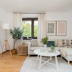 Przytulny salon, idealne **mieszkanie dla młodych**. Jasna sofa, stolik kawowy, rośliny i botaniczne plakaty tworzą relaksującą atmosferę.