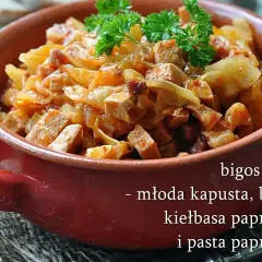 Pyszny bigos z młodej kapusty z boczkiem i kiełbasą paprykową, podany w glinianym naczyniu, udekorowany natką pietruszki.