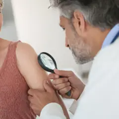 Dermatolog bada skórę pacjentki lupą, szukając oznak liszaja. Może to być początek leczenia maścią na liszaj.