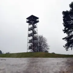 Wieża widokowa na górze lemana, z krętymi schodami i drewnianymi platformami, góruje nad zielonym wzgórzem.