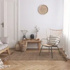 Un angolo del salotto arredato con un divanetto in legno, una poltrona in rattan, tappeto in juta e decorazioni naturali. Ecco come riempire un angolo del salotto con stile.