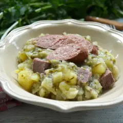 Herzhaftes Stielmus mit Kartoffeln und Wurst in einer Schüssel, daneben ein kariertes Tuch.