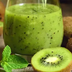Szklanka zielonego smoothie z kiwi, połówki kiwi i listki mięty na drewnianym tle.