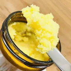 Ein Messer hebt eine Portion goldgelbes Ghee aus einem Glas. Dieses Ghee deutsch ist bereit für die Küche.