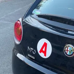 Autocollant "A" sur une Alfa Romeo noire, signe d'un jeune conducteur. La voiture a 140 ch.