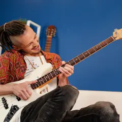 Mężczyzna z dredami gra na białej gitarze basowej. Ile strun ma gitara basowa? Ta ma cztery.