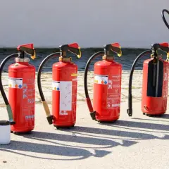 Różne rodzaje gaśnic stoją w rzędzie. Jedna jest rozcięta, ukazując wnętrze.