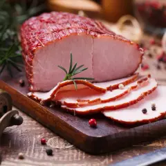 Pokrojona szynka wieprzowa na desce, ozdobiona rozmarynem i pieprzem. Idealna na kanapki, z niską zawartością szynka wieprzowa kcal.