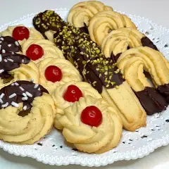 Vassoio di frolla montata: biscotti decorati con cioccolato, granella di pistacchio e ciliegie candite.