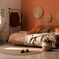 A cozy bedroom with bold colors like terracotta and rust. A bed with earthy-toned linens, a plant, and woven wall art.
