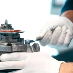 Mechanik w białych rękawiczkach dokręca śrubę przy turbosprężarce, być może regulując zawór N75.