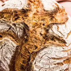 Händerna håller ett nybakat, fiberrikt bröd med en härlig skorpa.