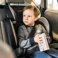 Chłopiec w foteliku antymandat, z książką w ręku, bezpiecznie podróżuje samochodem.