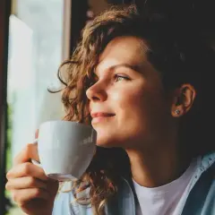 Frau mit lockigen Haaren genießt eine Tasse Chai Latte, ein Moment der Ruhe während der Schwangerschaft.