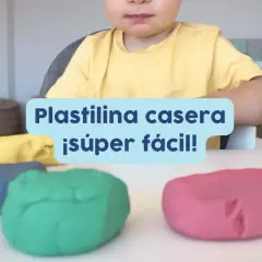 Un niño sonriente listo para jugar con plastilina casera para niños de colores: azul, verde, amarillo y rosa.